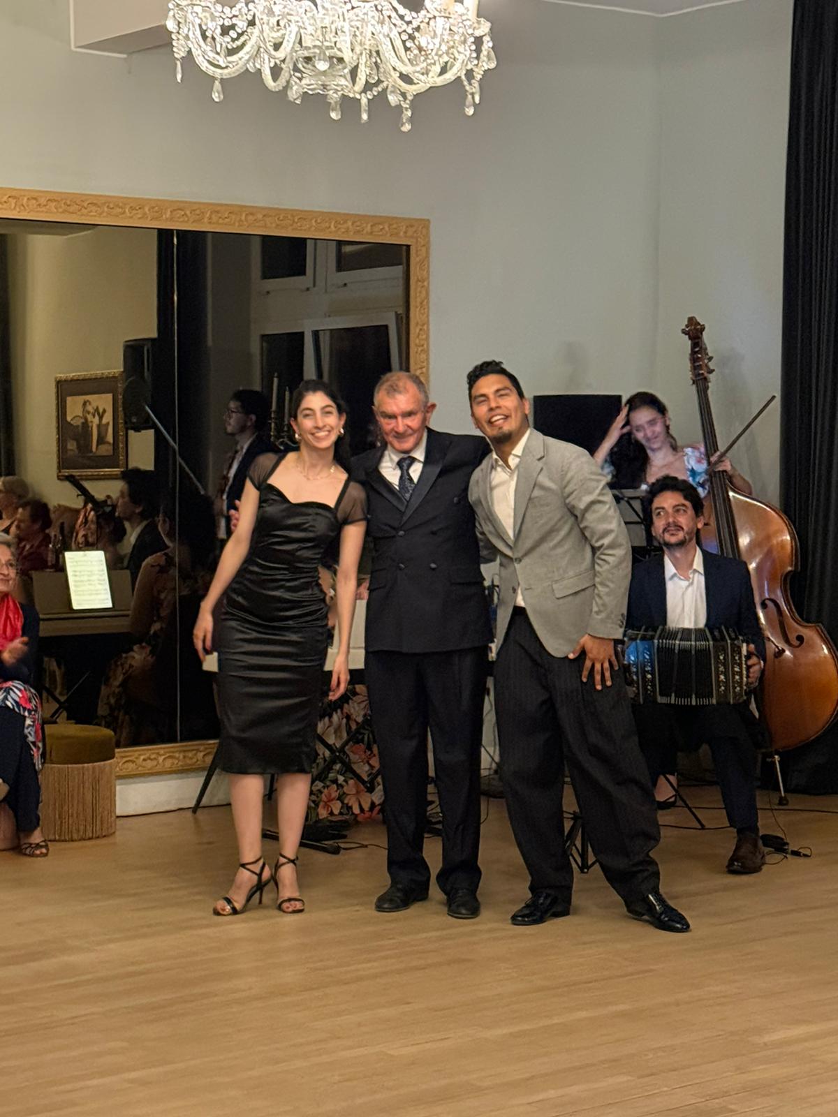 Three people posing on a dance floor at a formal event, with a live band visible in the background.