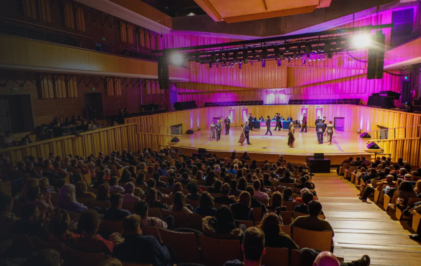 A bustling theater with a live performance on a lit stage and a large audience in the auditorium.